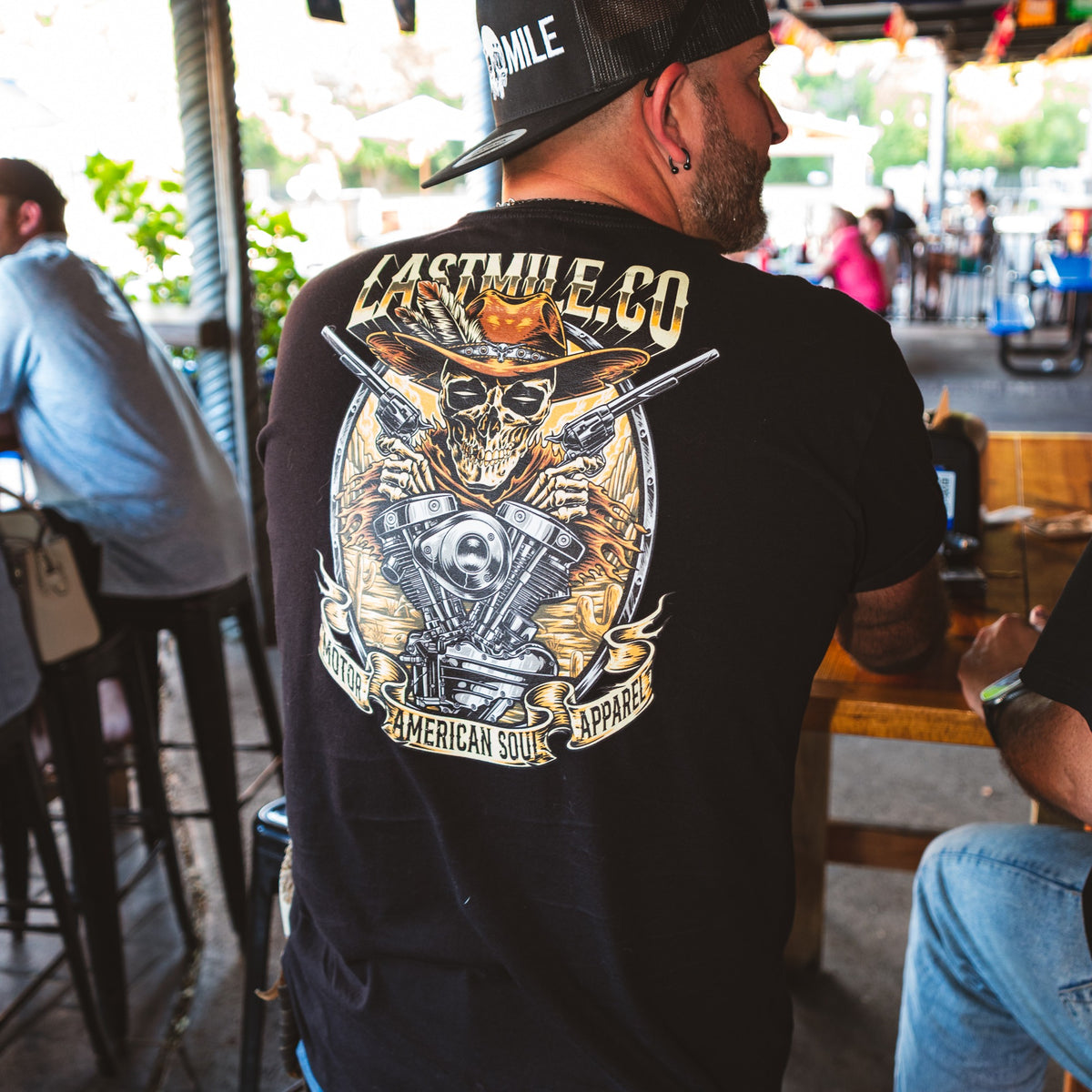 Built to Last Tee men's motorcycle t-shirt worn on a bar patio, back print shown on a rider