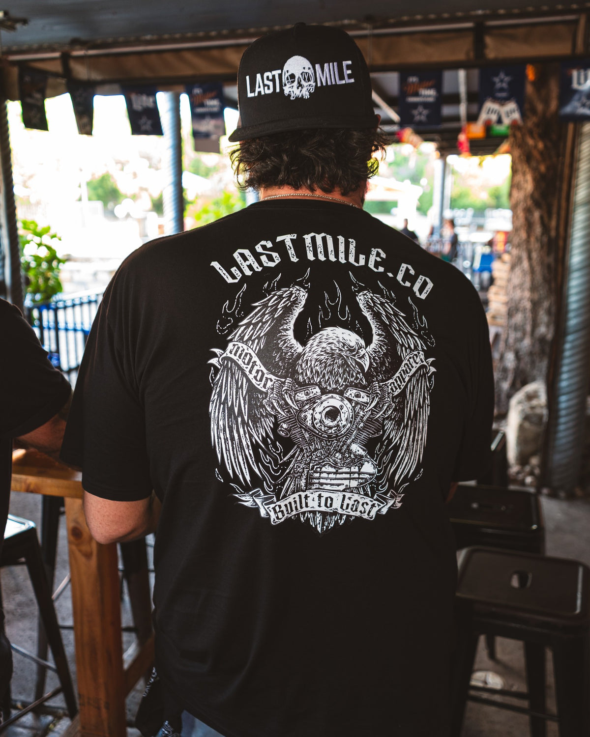 Wing and Iron Tee, worn by a rider, back graphic on a bar patio